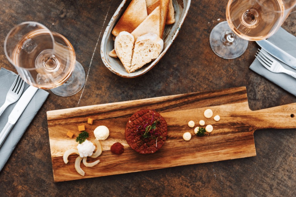 frisches Beef Tartar, serviert auf einem Holzbrett mit einem Glas Rosé