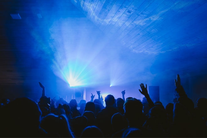 Menschen tanzen im Gegenlicht zu elektronischer Musik, umgeben von Lichtstrahlen und Nebel.